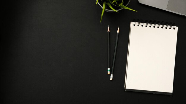 Black study table with empty spiral notepad pencils laptop decor plant and copy space top view