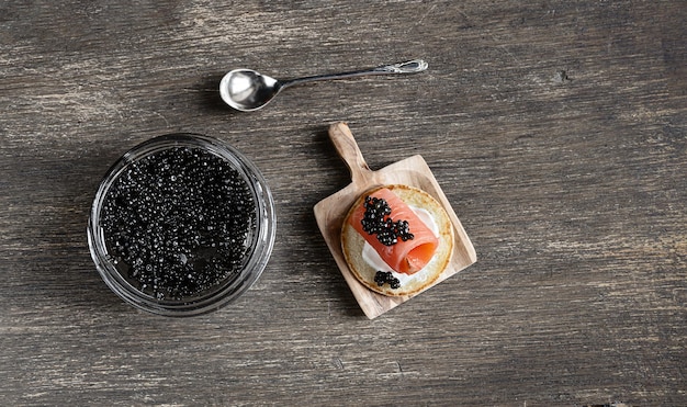 Black sturgeon caviar in a glass jar and a pancake with salmon and caviar on a wooden table