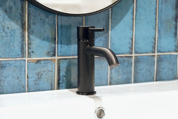 Black stylish metal bathroom faucet on the background of blue ceramic tiles