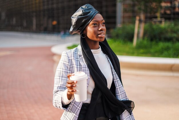 Donna nera alla moda con caffè da asporto nel parco cittadino