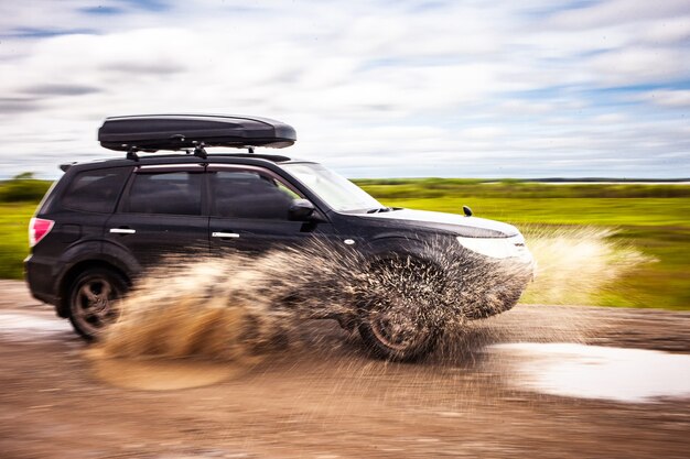 Черный Subaru Forester едет по грунтовой дороге с лужами. Брызги воды из-под колес. Размытость