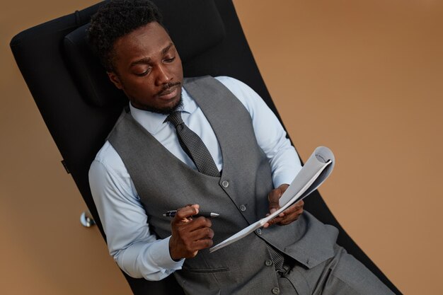 Black successful businessman reading document while lying in chair