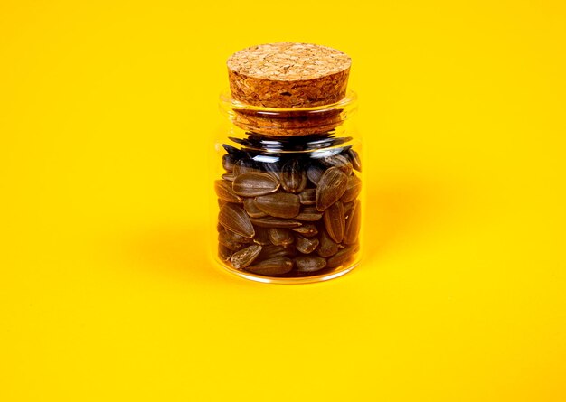 Black sunflower seeds in glass jar wine glass in bucket sunflower seeds on orange yellow background front view sunflower seeds