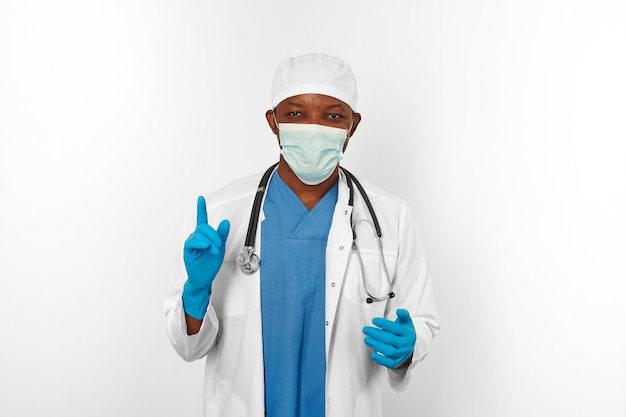 Black surgeon doctor man in white blue coat gloves white cap surgeon mask makes attention gesture