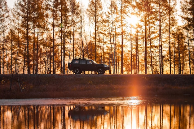 Black SUV on foreat road near a lake at sunset