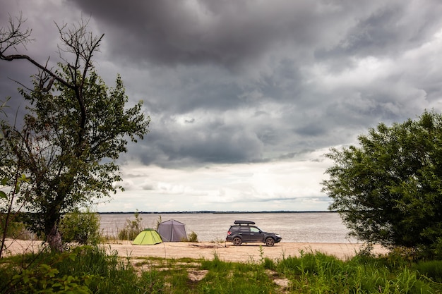 Black SUV with rooftop box near camping at the river.