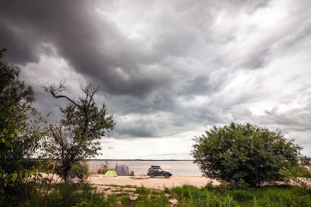 Black SUV with rooftop box near camping at the river.