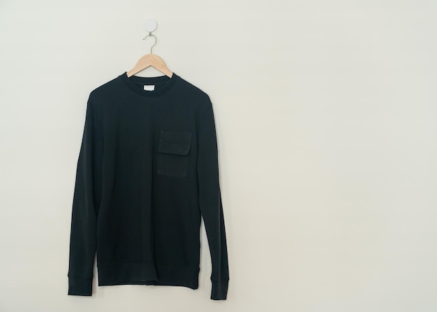 black sweater hanging with wood hanger on wall