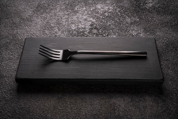 Черная столовая вилка на деревянном подиуме. стильный минималистичный натюрморт.