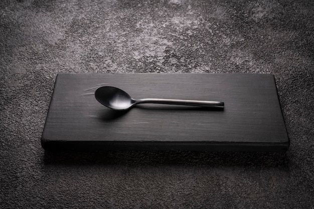 Черная столовая маленькая чайная ложка на деревянном подиуме. стильный минималистичный натюрморт.