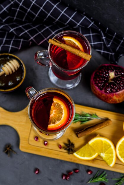 Foto un tavolo nero con due bicchieri di vin brulè, una stecca di cannella e una tazza di vin brulè caldo