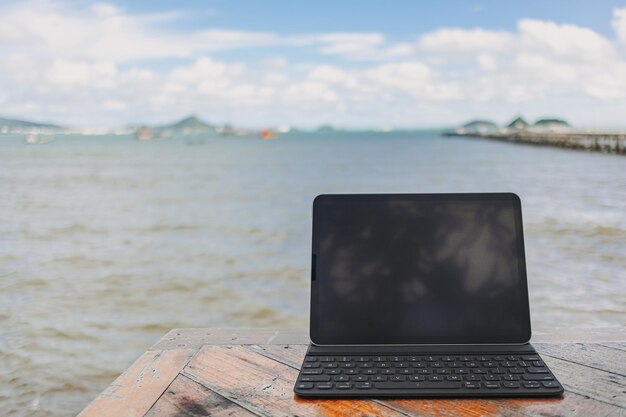 Black tablet with keyboard on table and sea view in concept of workation