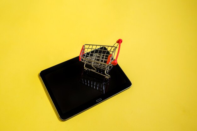 Black tablet with a metal cart on a yellow surface with a copy of the space