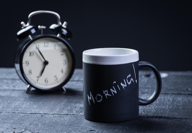 Black tea cup with alarm clock on wooden table