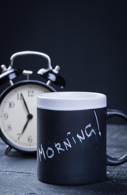 Black tea cup with alarm clock on wooden table