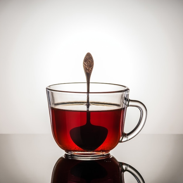 Foto tè nero in una tazza di vetro con manico e cucchiaino. foto scattata in studio