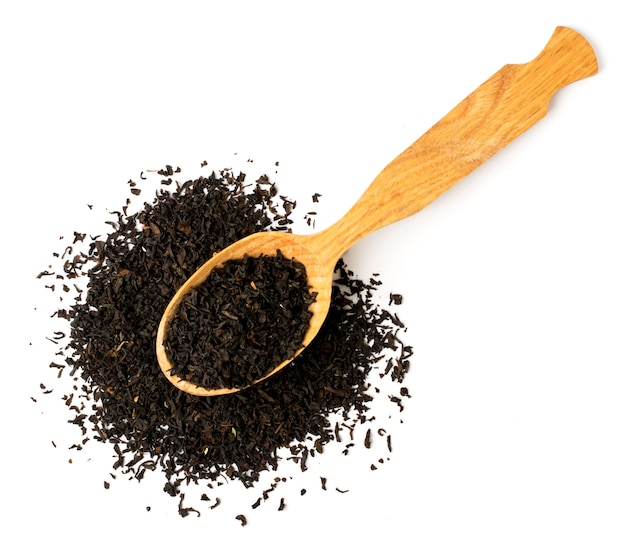 Black tea leaves in wooden spoon on white. Top view.