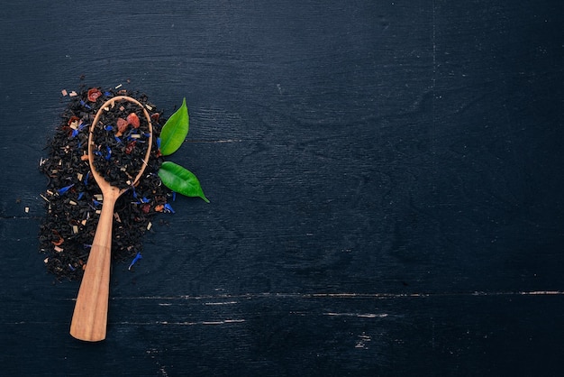 Black tea with flower petals of cornflower and dry berries On a wooden background Top view Copy space