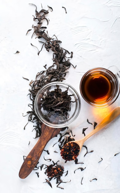 Черный чай с чаем в деревянной чаше и стеклянной чашке на белом фоне