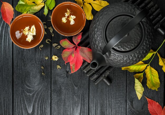 Black teapot and green tea with jasmine in a clay cup, on a black and wooden  with autumn leaves Food  Top view