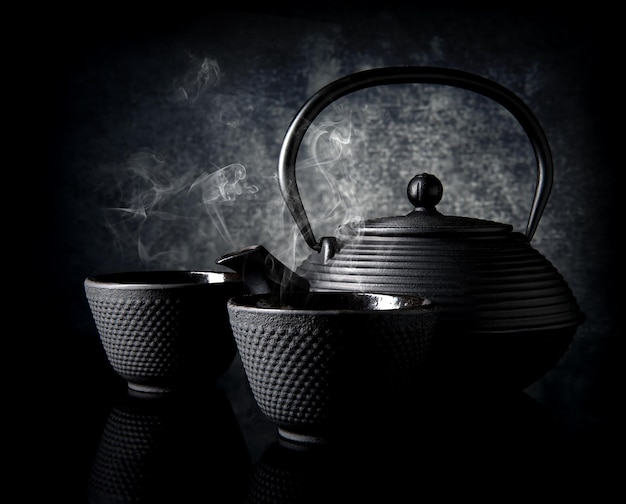 Черный чайник с маленькими чашками на черном фоне