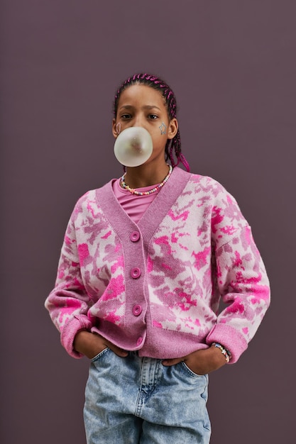 Foto adolescente nero che soffia bolla di gomma da masticare che guarda l'obbiettivo in studio