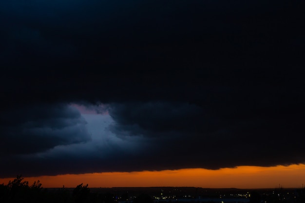 写真 日没時の黒い雷雲。明るいオレンジ色の夕日と暗い雲。嵐の空