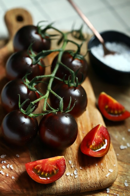 Фото Черные помидоры на ветке на деревянной доске с морской солью