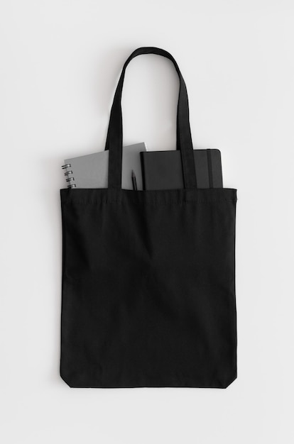 Foto mockup di borsa tote nera con quaderni su un tavolo bianco