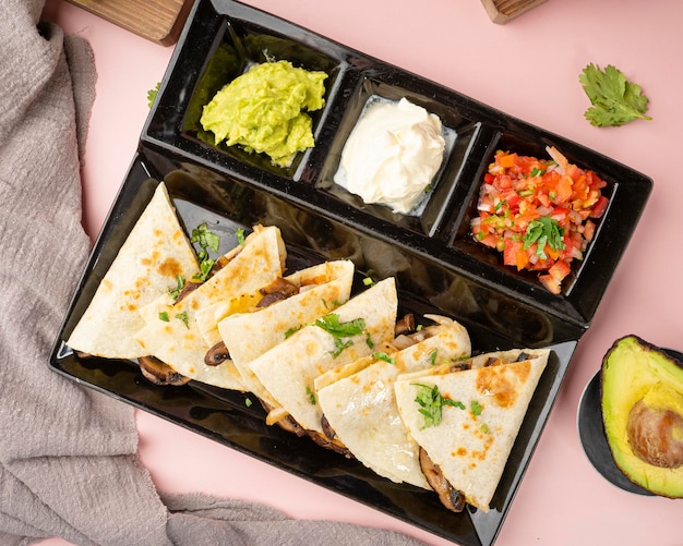 Foto un vassoio nero con una varietà di cibi tra cui quesadillas, guacamole e guacamole.