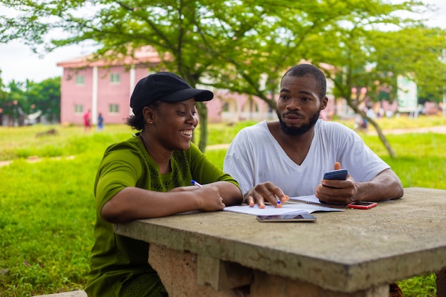 Black university handsome man assisting his female friend with her lecture in the campus. Focus is on student.