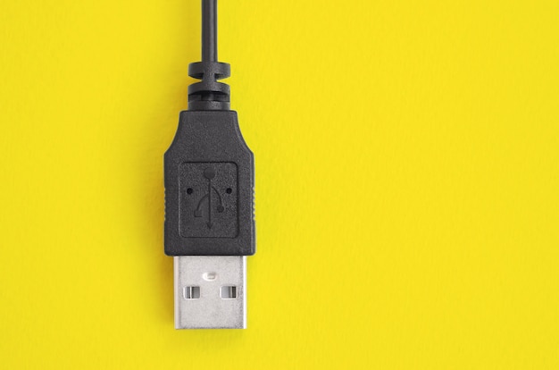 Black USB plug lies on a bright yellow background.