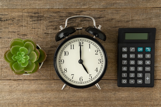 Black vintage alarm clock and calculator on a wooden background