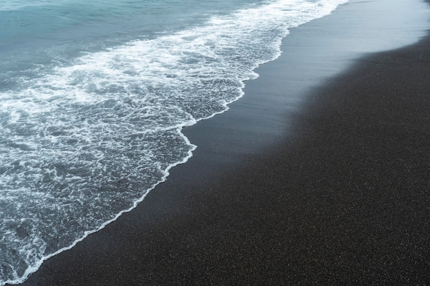 Black volcanic sand on the beach with waves