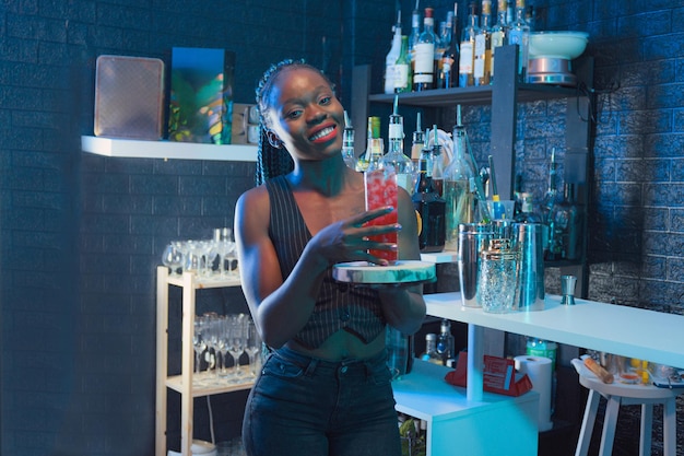 Photo black waitress show a cocktail on the bar of a pub looking at the camera