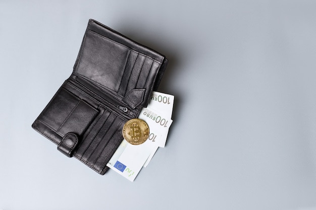 Foto un portafoglio nero con bitcoin oro ed euro su sfondo grigio. criptovaluta e scambio elettronico