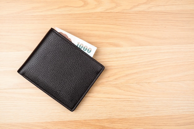 Black wallet with money on brown wood table background