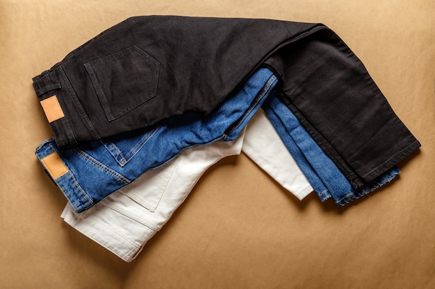 Photo black white blue jeans pants. assortment of different color denim clothing in store shop with emty label. white denim jean pants, blue jeans, black denim on brown table.