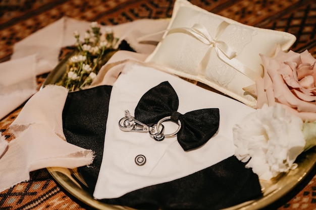 A black and white bow tie sits on a tray with a white pillow and a white pillow.