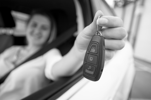 開いているウィンドウから車のキーを示す幸せな女性の黒と白のクローズアップ写真