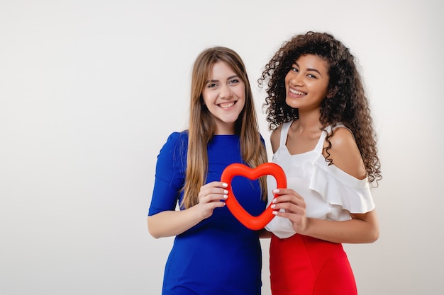 Black and white girlfriends with heart shaped figure smiling isolated