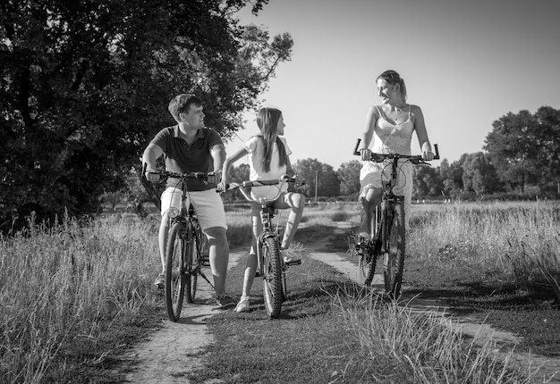 Black and white image of cheerful young family riding on bicycles at meadow