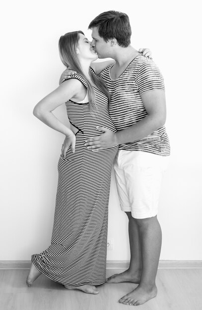Black and white image of happy kissing pregnant woman and husband in striped summer clothes
