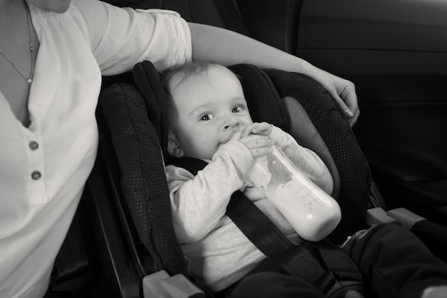 Black and white image of mother feeding baby from bottle in car