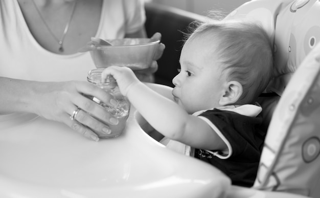 Black and white image of mother feeding her baby on kitchen