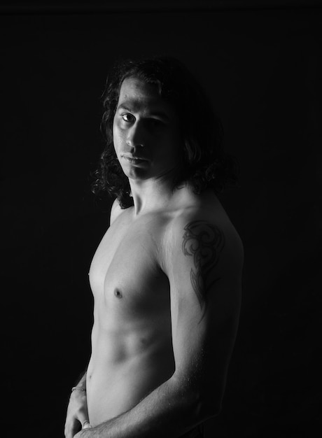 Black and white od low key portrait of shirtless man looking at camera black background