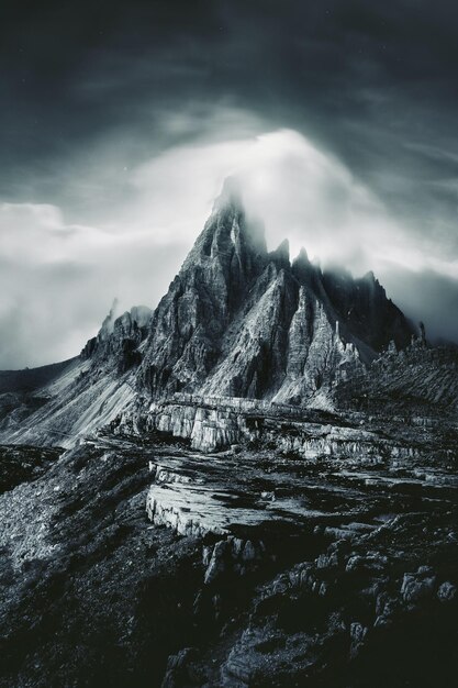 A black and white painting of a mountain with a dark sky and clouds.