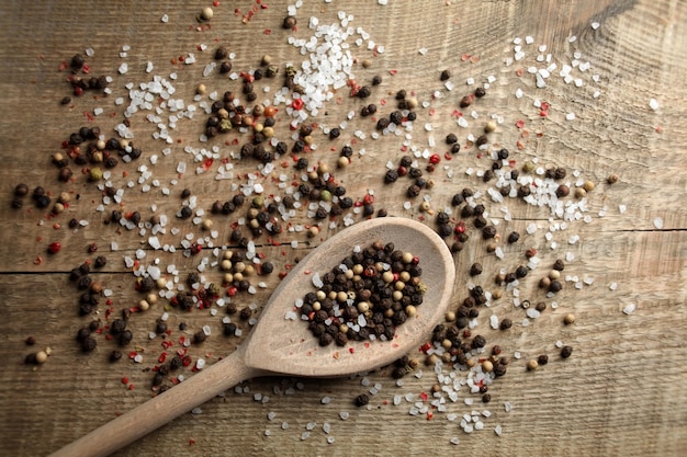Black and white pepper peas sea salt cloves spices in a spoon\
on a wooden background