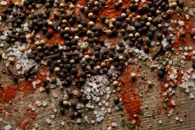 Black and white pepper peas sea salt cloves spices in a spoon\
on a wooden background