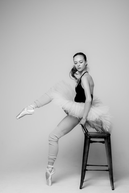 Black and white photo of a ballerina. Ballerina is sitting on a chair doing stretching for legs.